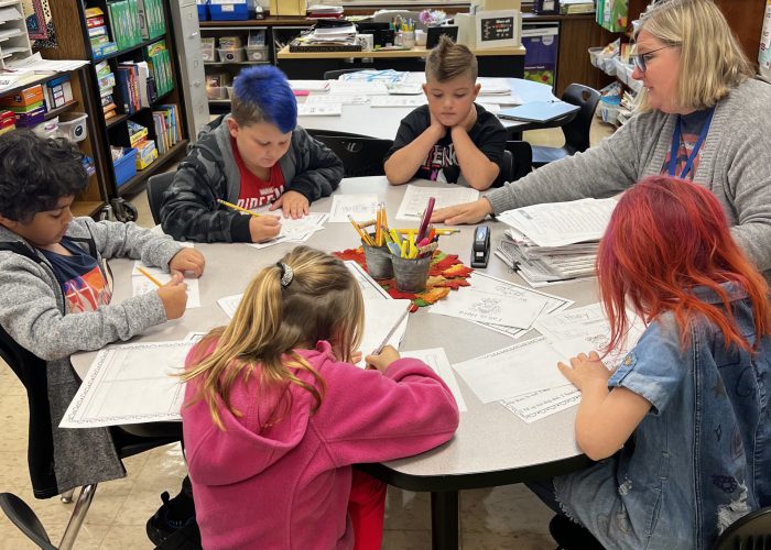 Students and teacher sitting at round table working on classwork