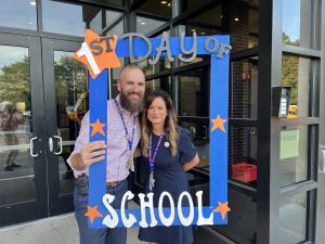Two people pose with a first day of school frame