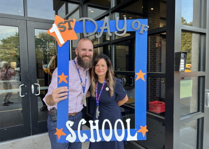 Two people pose with a first day of school frame