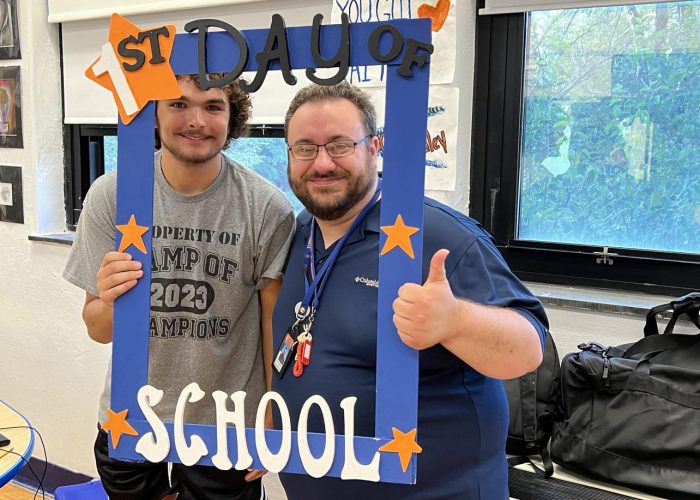 Two people pose with a first day of school frame