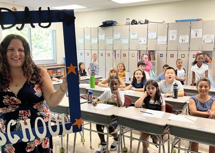 A teacher holds a First Day of School frame with her class around her