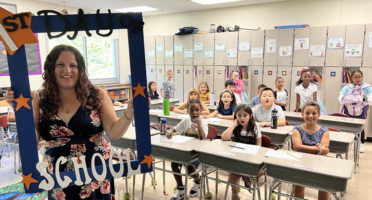 A teacher holds a First Day of School frame with her class around her