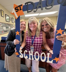 Three people hold a first day of school frame