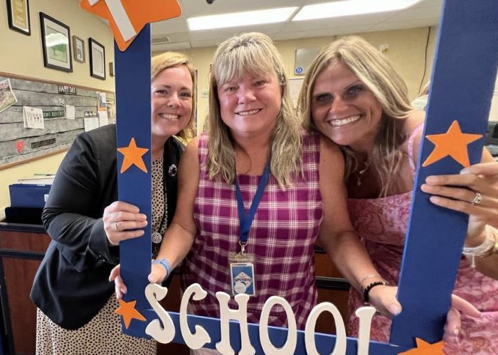 Three people hold a first day of school frame