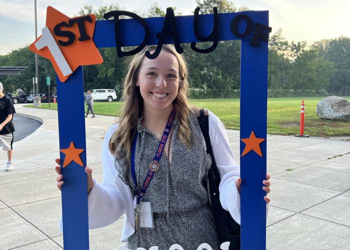 A teacher poses with a first day of school frame