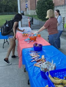 A student grabs a bottle of water from a table lined with breakfast foods as two other people stand behind the table