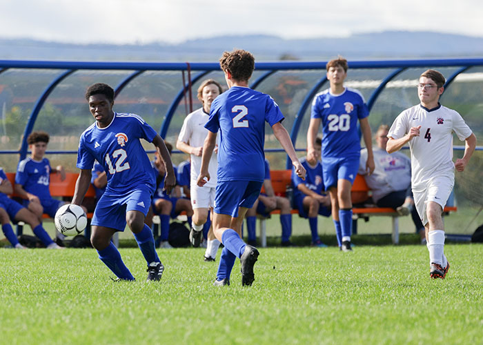 Three soccer players in blue look to move the ball up the field
