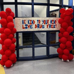 A banner, with messages and signatures, flanked by red balloons reads be kind to your mind live drug free.