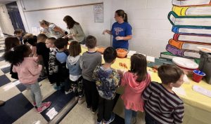 Adults stand on one side of a table by while students sit on the other side