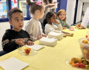 Sstudents sit at a table with adults behind them.