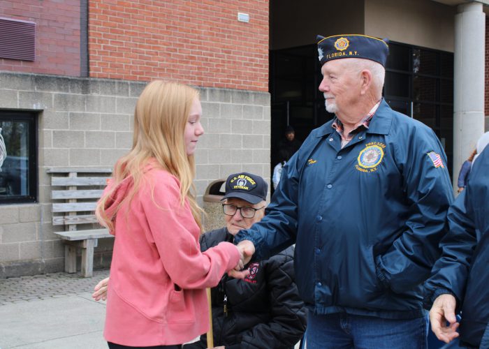 Student shaking hands with a veteran in front of school building