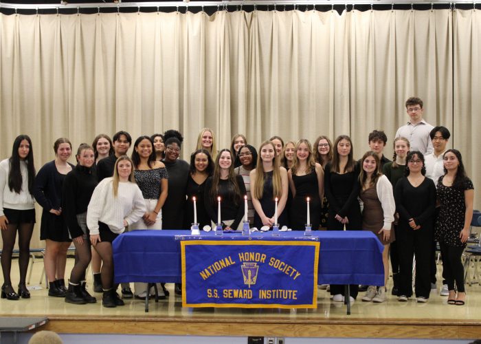 NHS Students pose on stage for a photo behind their banner