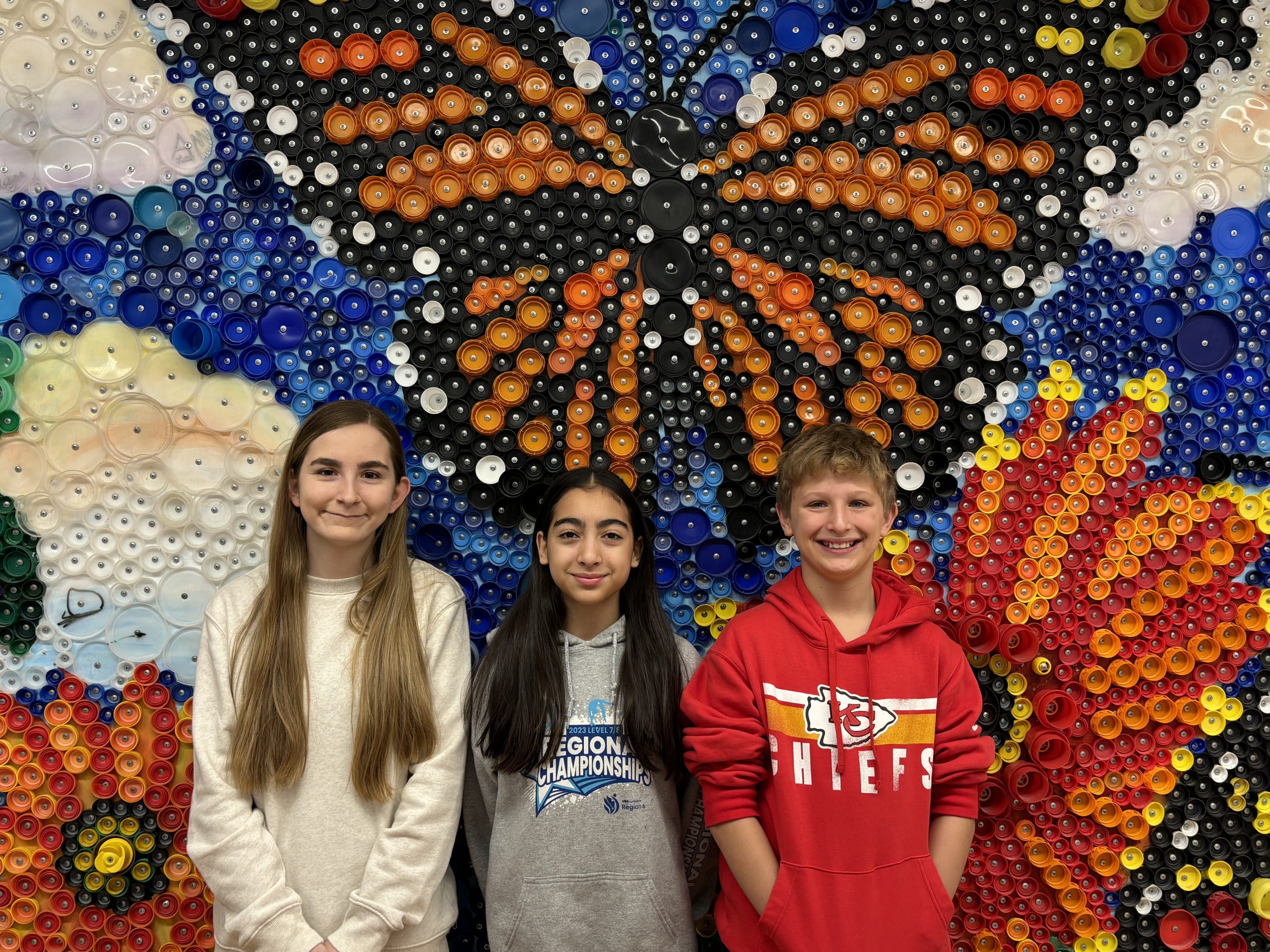 3 students pose in front of mural