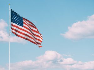 An American flag flies in a bright blue sky with some clouds.