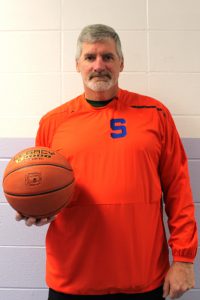coach steele smiles for the camera and holds a basketball