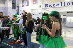 Students dressed in green hand out bead necklaces to students for rock paper scissors tournament