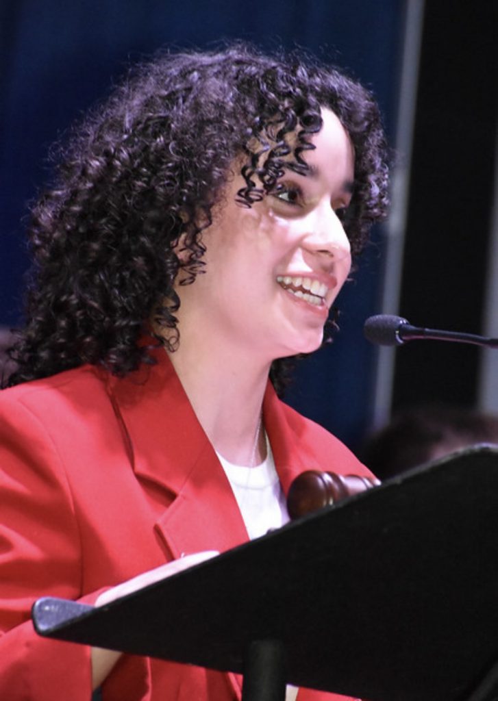 Student in red blazer speaking at podium