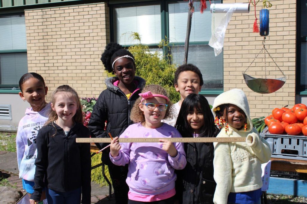 Students pose with ruler in front of vegetable stand